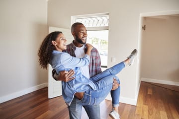 Happy couple celebrating in their new home, with the man lifting the woman in a joyful embrace