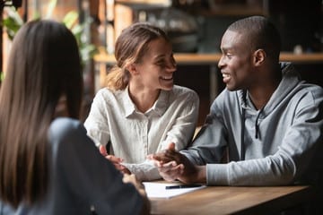 Smiling couple sitting at a table discussing paperwork with a professional