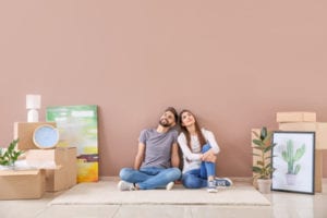 Young couple sitting on the floor of their new home surrounded by moving boxes and framed artwork