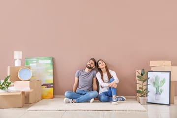 Young couple sitting on the floor of their new home surrounded by moving boxes and framed artwork