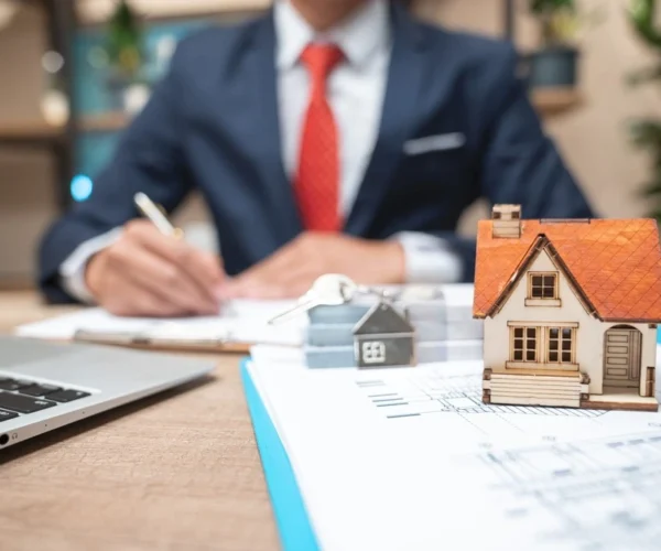 Businessman in suit writing on paper with house model for Ace Mortgage Loan Corporation.