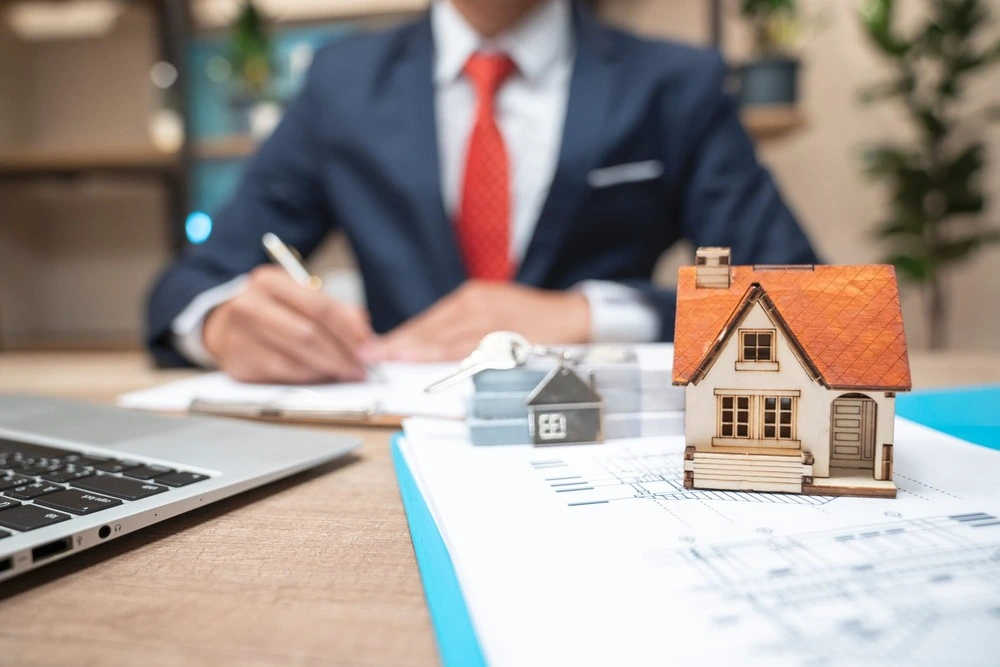 Businessman in suit writing on paper with house model for Ace Mortgage Loan Corporation.